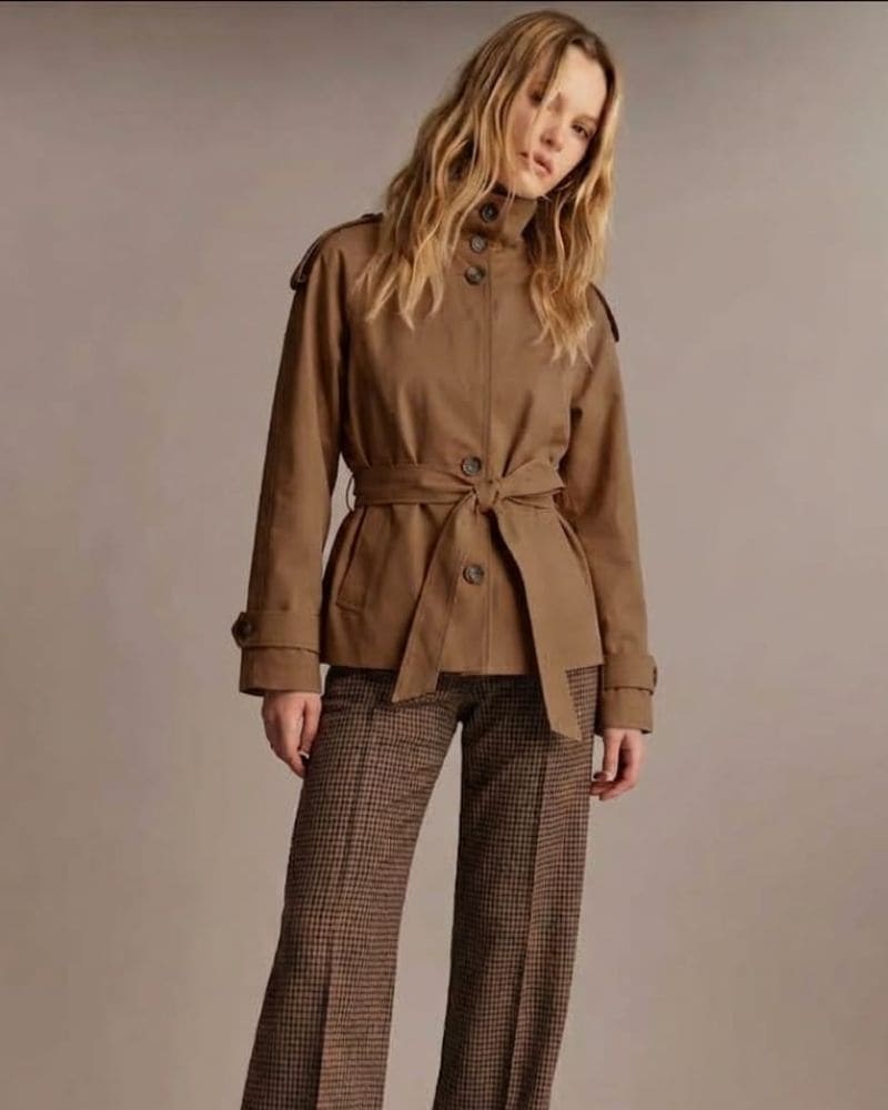 Model wearing a brown structured trench jacket with tie belt over checked trousers